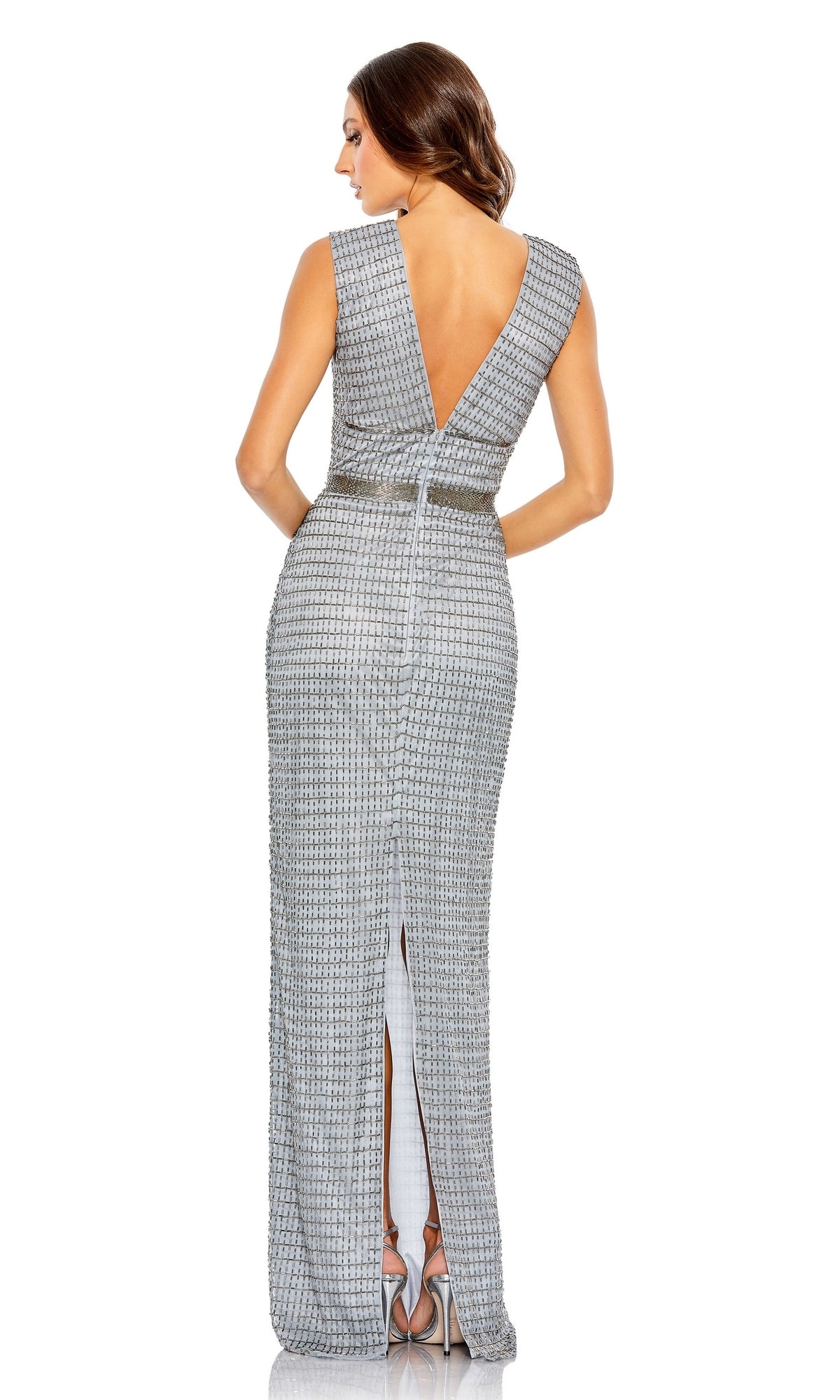 A woman in a sleeveless, silver Mac Duggal 5625 V-neck long beaded formal dress with a deep V-back and back slit stands facing away from the camera.
